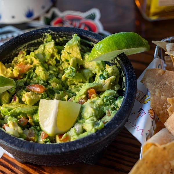 Fresh guacamole with lime wedges in a dark bowl, served with tortilla chips.