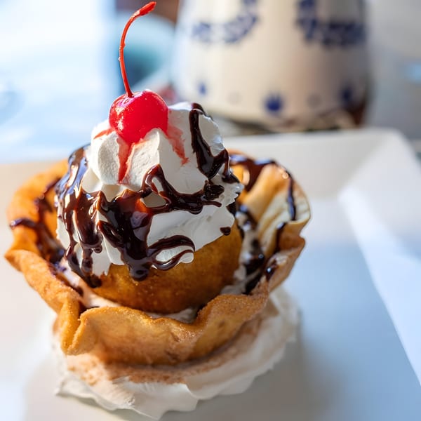 Fried ice cream dessert with whipped cream, chocolate syrup, and a cherry on top.