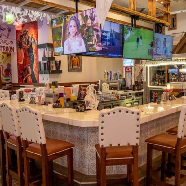 A vibrant bar area at Pedros Tacos & Tequila Bar, featuring a long counter with stools and multiple TVs.